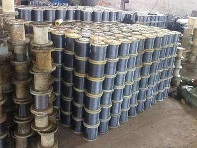 There are many spools of black iron wires stacked up and placed in a warehouse.